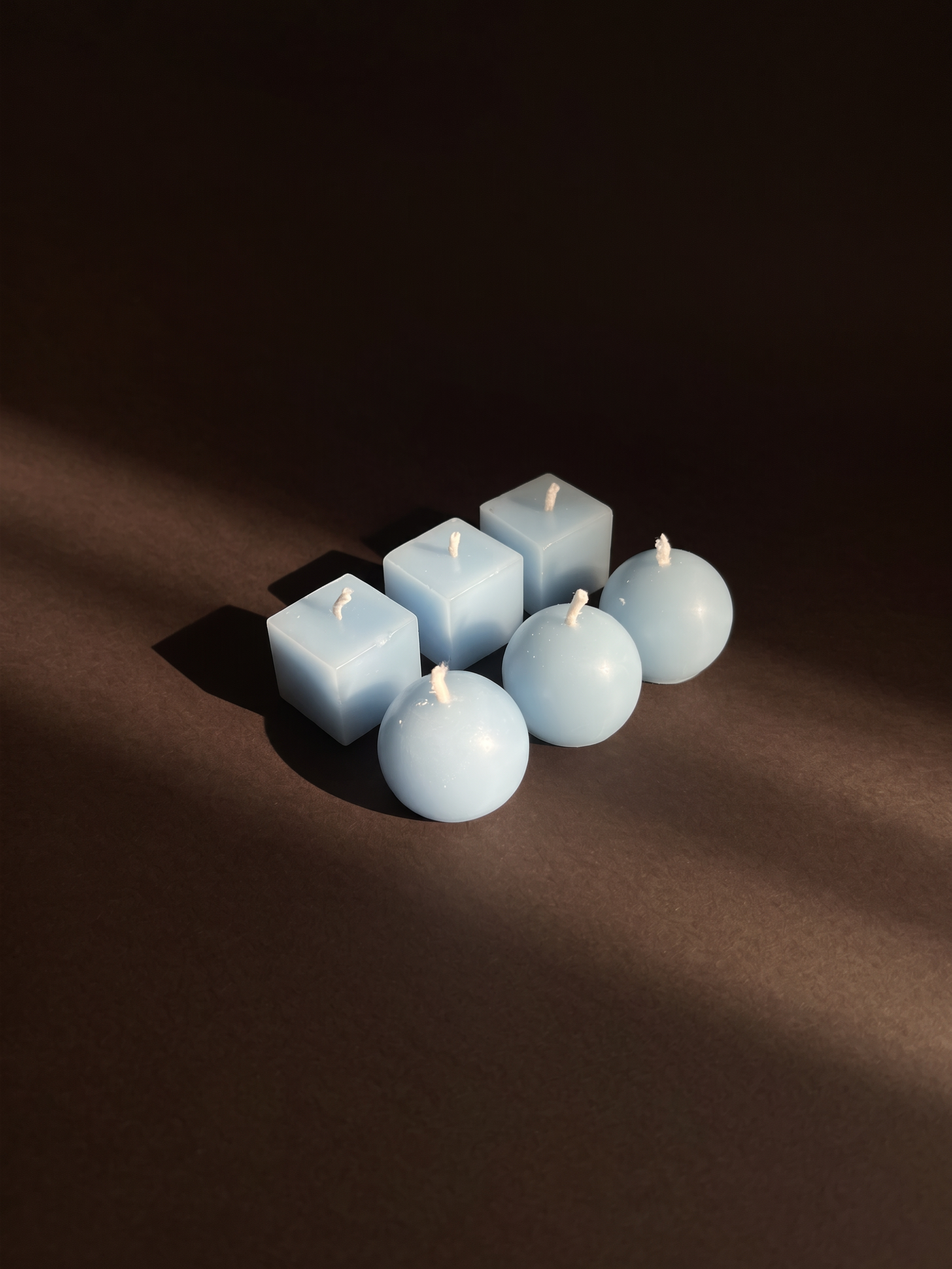 Six pale blue Aritual scented timer candles, three cubes and three spheres, in a shaft of light