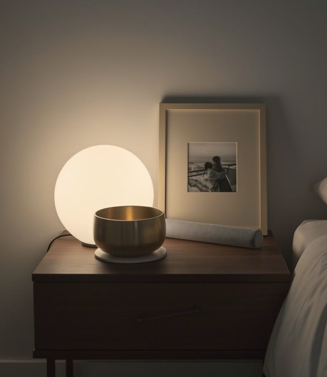 Evening reset — brass singing bowl and mallet on a bedside table under lamplight