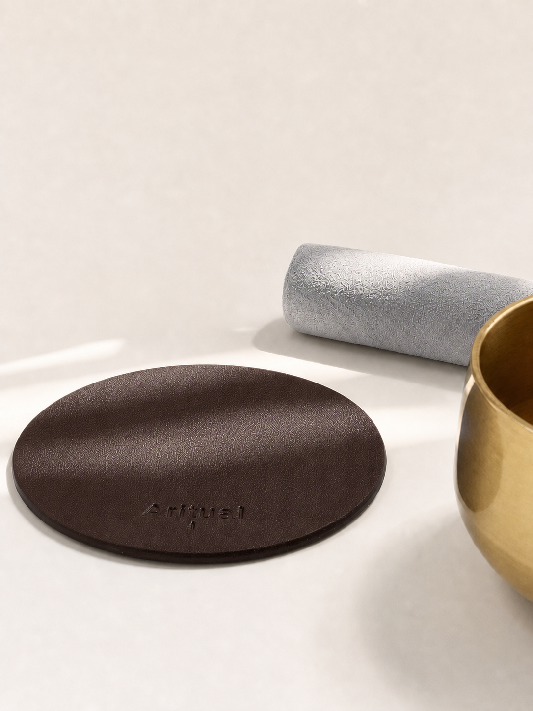 Deep brown leather pad beside the brass singing bowl and suede mallet